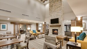 A spacious hotel lobby with a stone fireplace, comfortable seating, and a flat-screen TV mounted on the wall. - King Studio w/ Kitchen | Pool + Daily Breakfast (Oklahoma City)