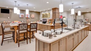 A hotel kitchen with a breakfast bar, a sign for free daily breakfast, and a variety of breakfast items. - King Studio w/ Kitchen | Pool + Daily Breakfast (Oklahoma City)