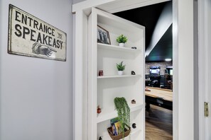 Ein Büro mit einem weißen Bücherregal, einem Schild mit der Aufschrift 'ENTRANCE TO SPEAKEASY' und einem Billardtisch.