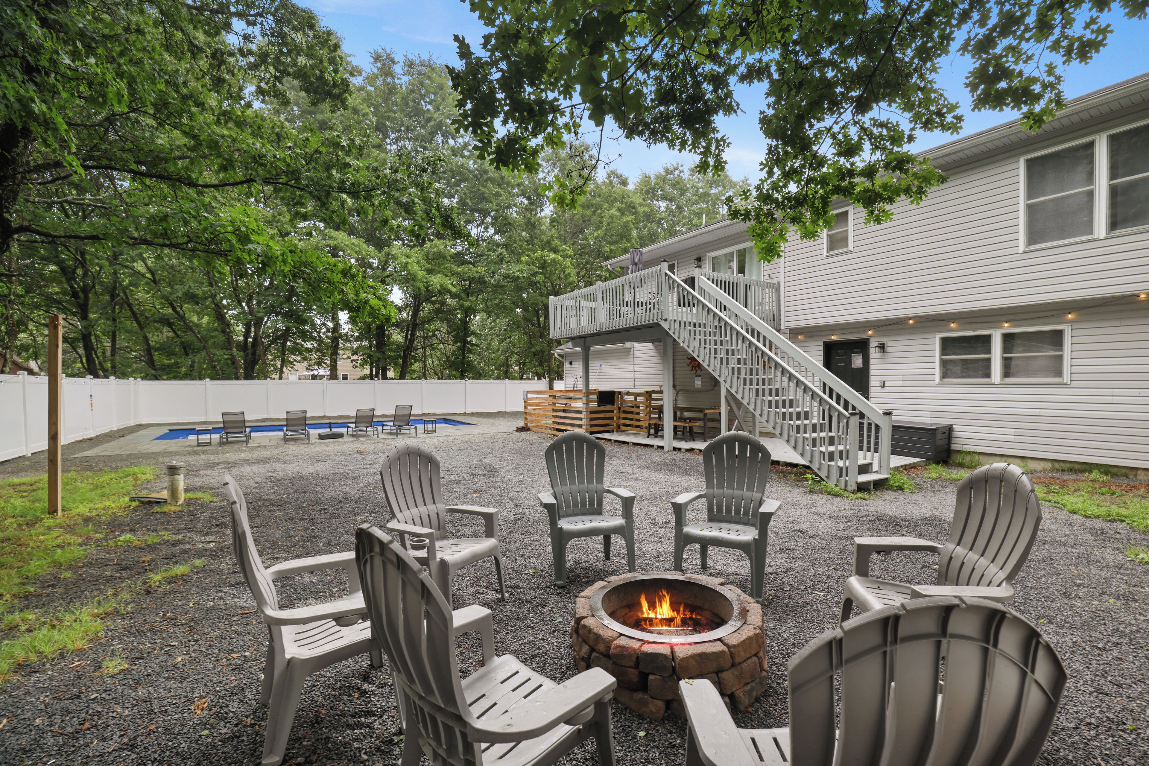 Ein Garten mit Feuerstelle, Sitzgelegenheiten im Freien, einem Pool und einem Haus mit Treppe.