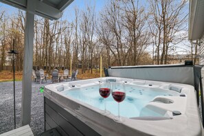 Ein Whirlpool mit zwei Weingläsern, umgeben von Bäumen und Gartenmöbeln.
