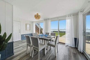 Un comedor con una mesa preparada para cuatro, una escalera y ventanas amplias con cortinas.