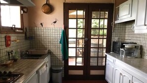 A kitchen with white cabinets, a stove, a trash bin, and a window with a view of greenery. - Country house with swimming pool  (Savenès)