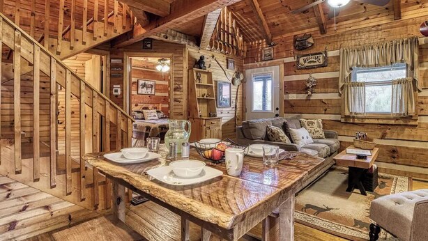 A wooden cabin interior with a dining area, a staircase, a living room, and a ceiling fan. - Cozy 2-bedroom cabin in beautiful Sevierville with fishing pond (Sevierville)