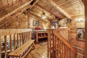 Eine Holzhütte mit Schlafzimmer im oberen Bereich, einer Holztreppe und einem Fenster mit Blick auf einen Bären.