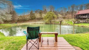 A fishing area with a chair, a table, and fishing rods by a calm pond. - Cozy 2-bedroom cabin in beautiful Sevierville with fishing pond (Sevierville)