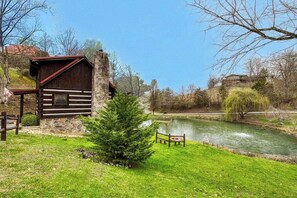 Ein rustikales Blockhaus mit Steinuntergrund, einer Holzdiele und einem Teich im Hintergrund.
