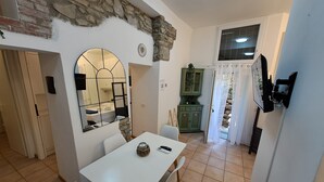 A dining area with a white table, chairs, a stone wall, a mirror, and a view into the kitchen. - Manarola Sunset House | 2 Bathrooms | In the Heart of Cinque Terre (Manarola)
