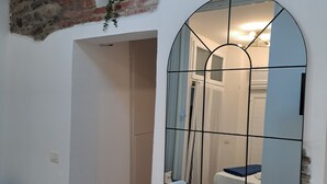 A room with a stone wall, a white table, a mirror, and a door leading to another room. - Manarola Sunset House | 2 Bathrooms | In the Heart of Cinque Terre (Manarola)