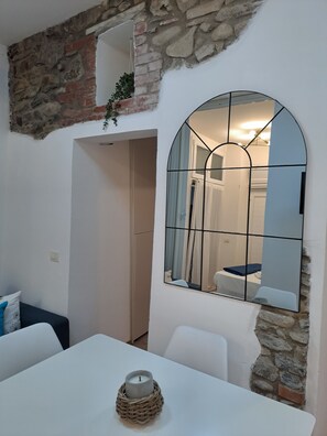 A room with a stone wall, a white table, a mirror, and a door leading to another room. - Manarola Sunset House | 2 Bathrooms | In the Heart of Cinque Terre (Manarola)