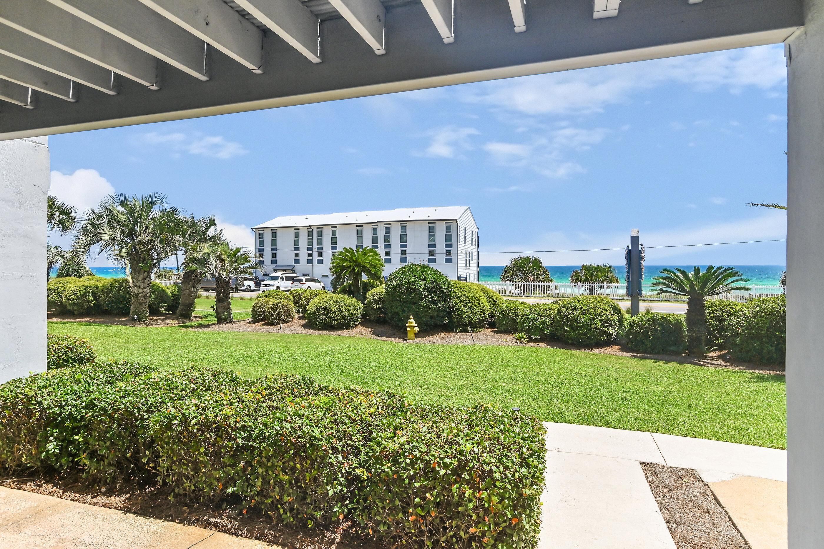 A building with a white facade, surrounded by well-maintained greenery and a clear view of the ocean.