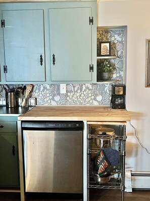 A kitchen with light blue cabinets, a dishwasher, a coffee maker, and a patterned backsplash.