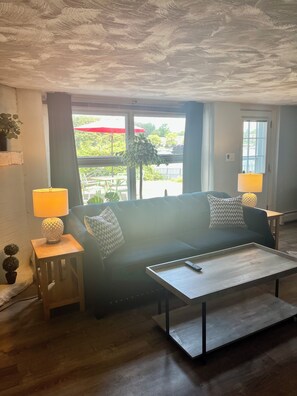 A living room with a sofa, two lamps, a coffee table, and a view of the outdoors.