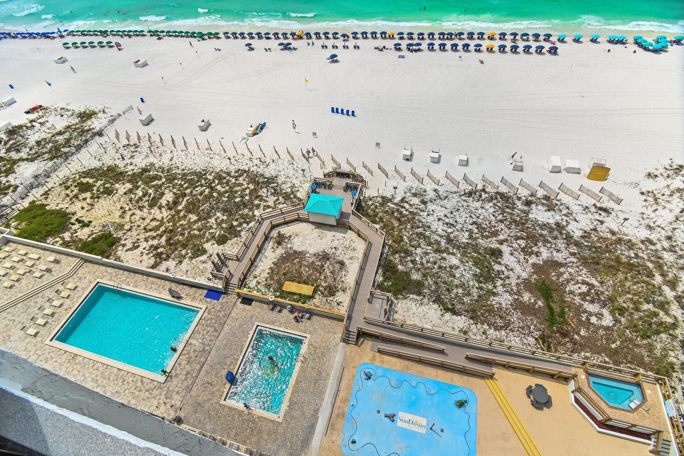 An aerial view of a beach resort with multiple swimming pools, beach umbrellas, and lounge chairs.