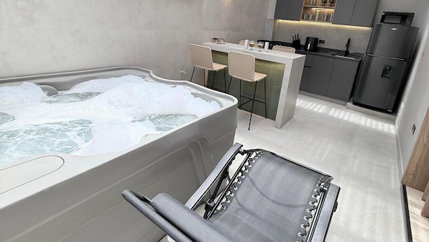 Un baño moderno con una bañera grande, zona de ducha y un espacio de descanso con una silla.