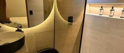 A modern bathroom with a round mirror, a black toilet, and a shelf with toiletries.
