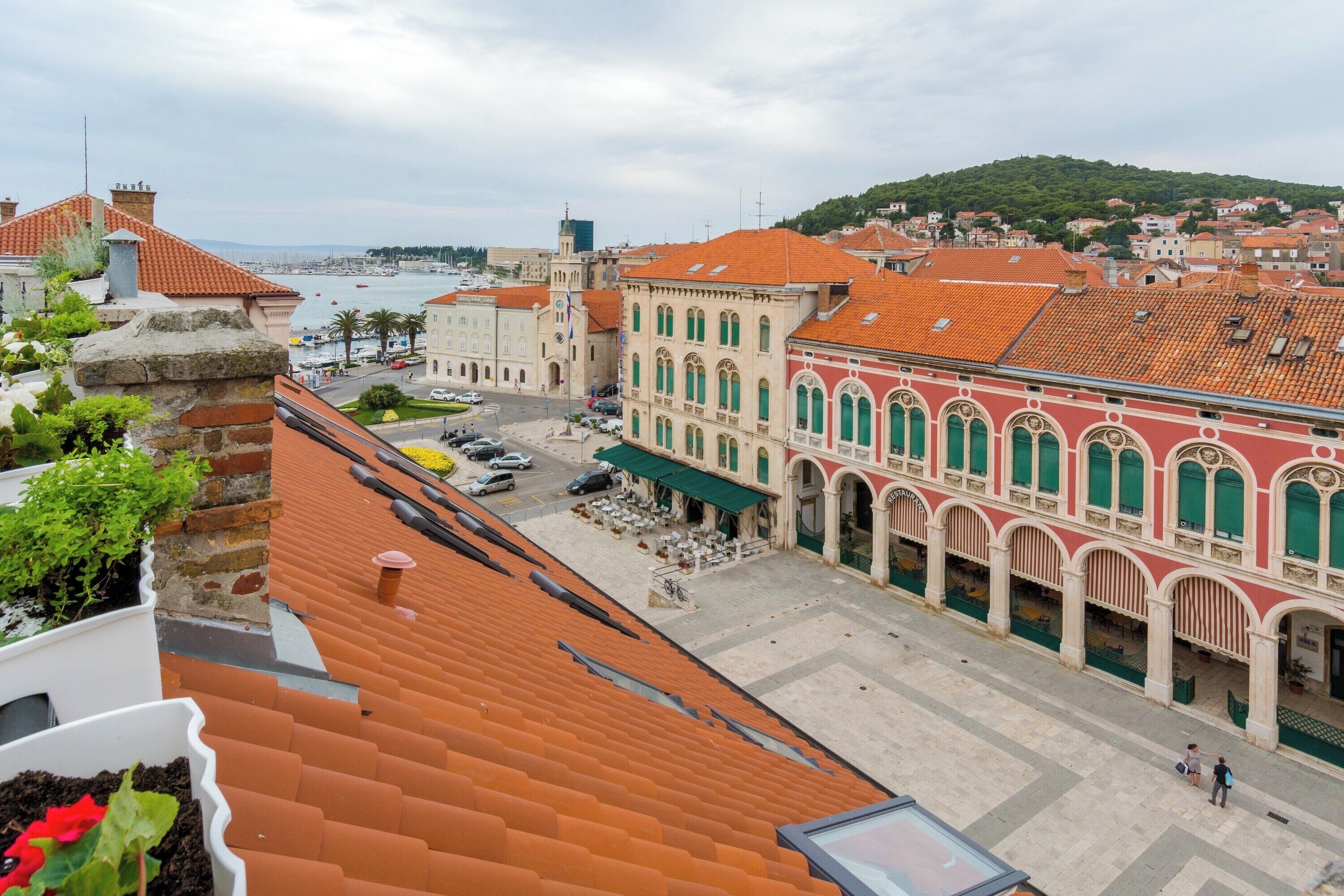 A historic building with a courtyard, a port in the background, and a view of the sea.