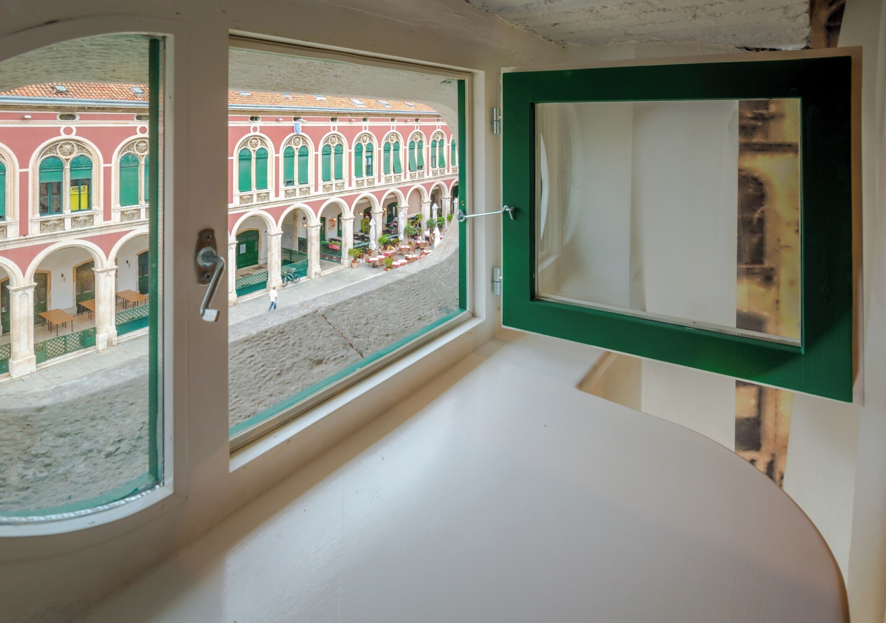 A room with a view of a red building with arches and a balcony.