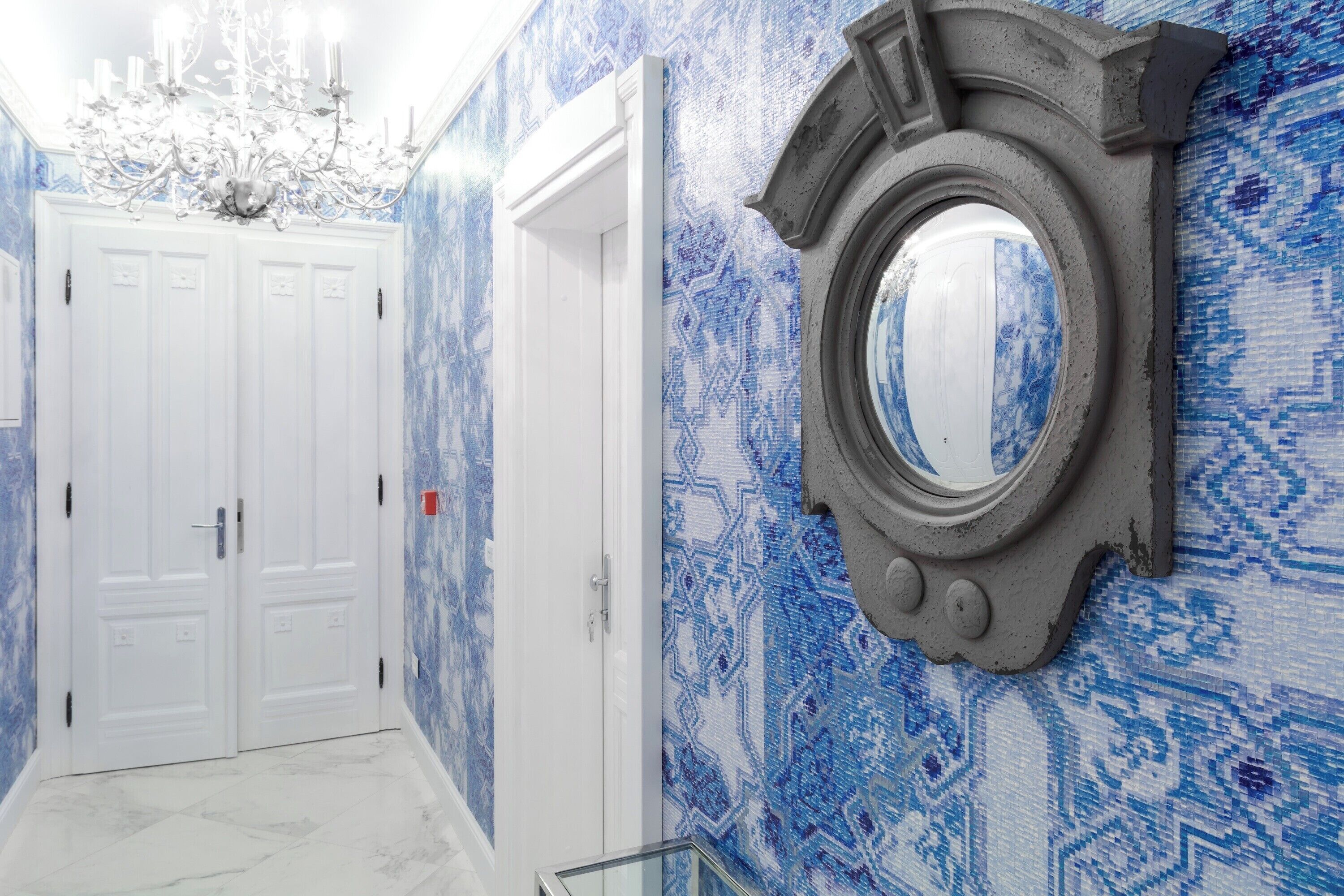 A hallway with patterned blue walls, a white door, and a round mirror.