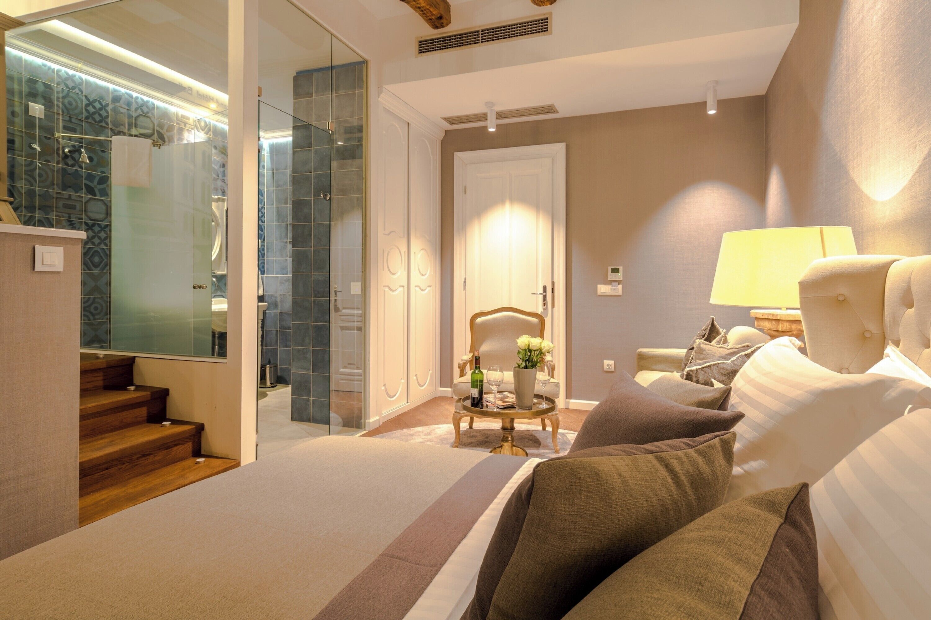 A hotel room with a bed, a chair, a lamp, and a bathroom with a shower and glass door.