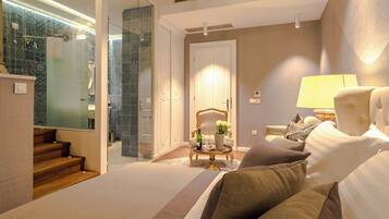A hotel room with a bed, a chair, a lamp, and a bathroom with a shower and glass door.