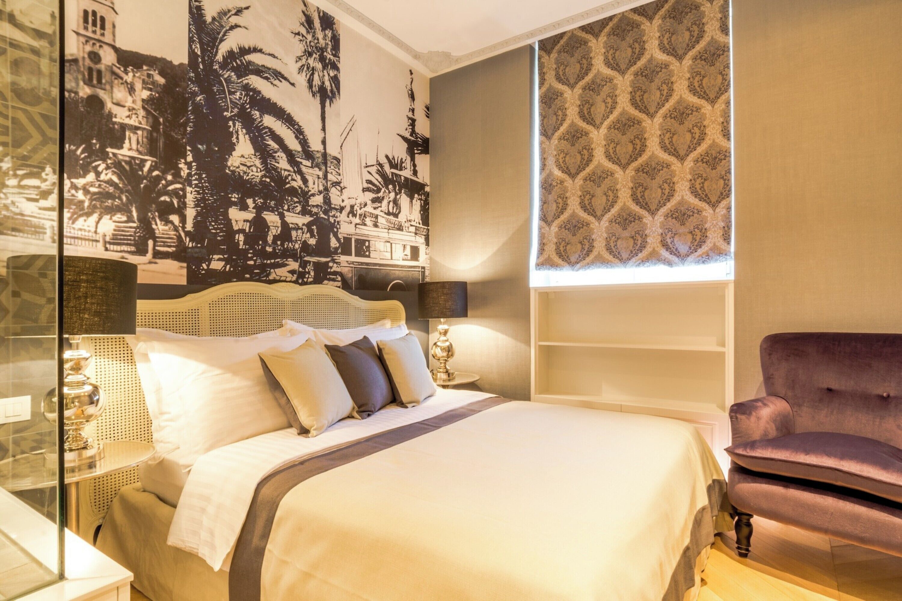 A hotel room with a bed, a chair, a wall tapestry, and a patterned window blind.