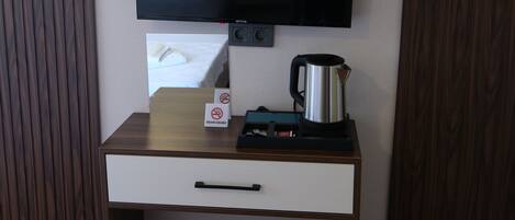 Una habitación con una televisión de pantalla plana montada en la pared, un pequeño escritorio de madera con cajón, una cafetera y un termostato.
