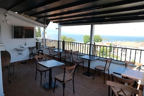 Une terrasse extérieure avec des tables et des chaises, un téléviseur fixé au mur et une vue sur la mer.