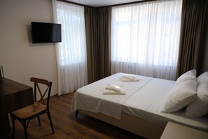 A hotel room with a bed, a TV mounted on the wall, a wooden chair, and a desk.