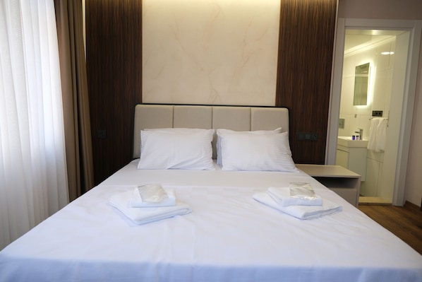 Une chambre d’hôtel avec un lit, deux oreillers, une table de chevet et une salle de bain visible à travers une porte ouverte.