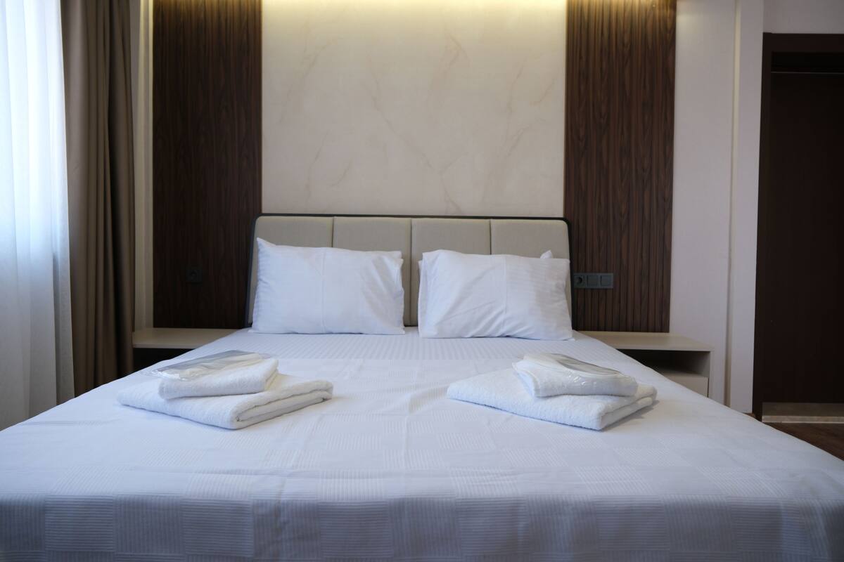 Una habitación de hotel con una cama grande, dos almohadas y dos toallas dobladas con cuidado.