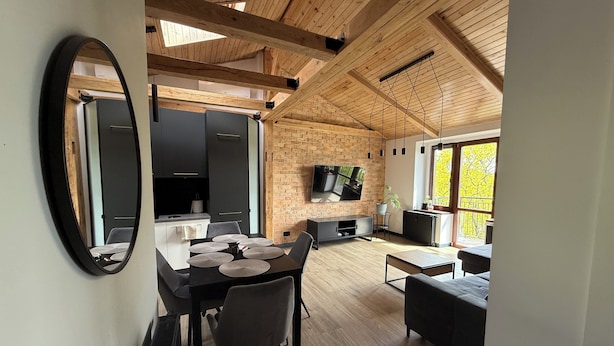 Een modern interieur met een eetgedeelte, keuken en woonruimte, met zichtbare houten balken, een grote televisie en uitzicht op het omliggende landschap.