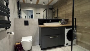 Een moderne badkamer met toilet, wastafel, spiegel en een wasmachine.