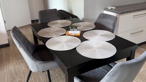 Een eetruimte met een zwarte tafel, grijze stoelen en een witte muur met een ronde spiegel.