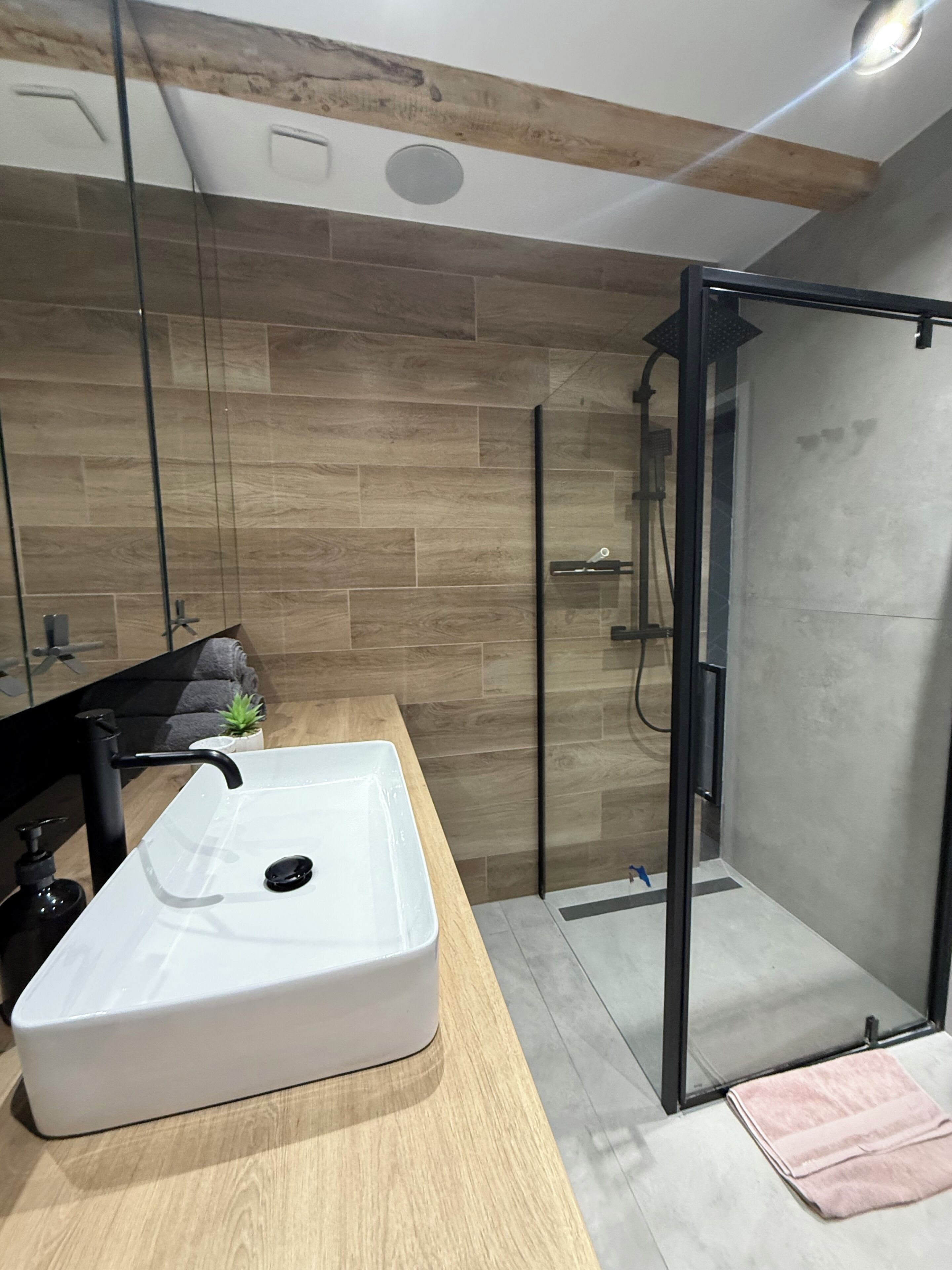A modern bathroom with a large white sink, a glass shower enclosure, and a wooden wall.