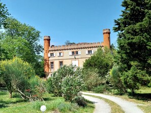 A historic building with a central tower, surrounded by lush greenery and a gravel path. - Le Gite de Douine (Avignonet-Lauragais)