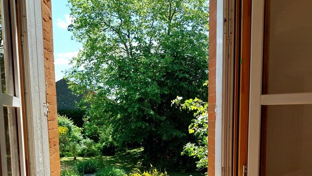 Een open deur met uitzicht op een tuin en een balkon met balustrades.