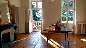 Een kamer met houten vloeren, een open haard, een tafel met een vaas en een uitzicht door een geopende deur naar een balkon.