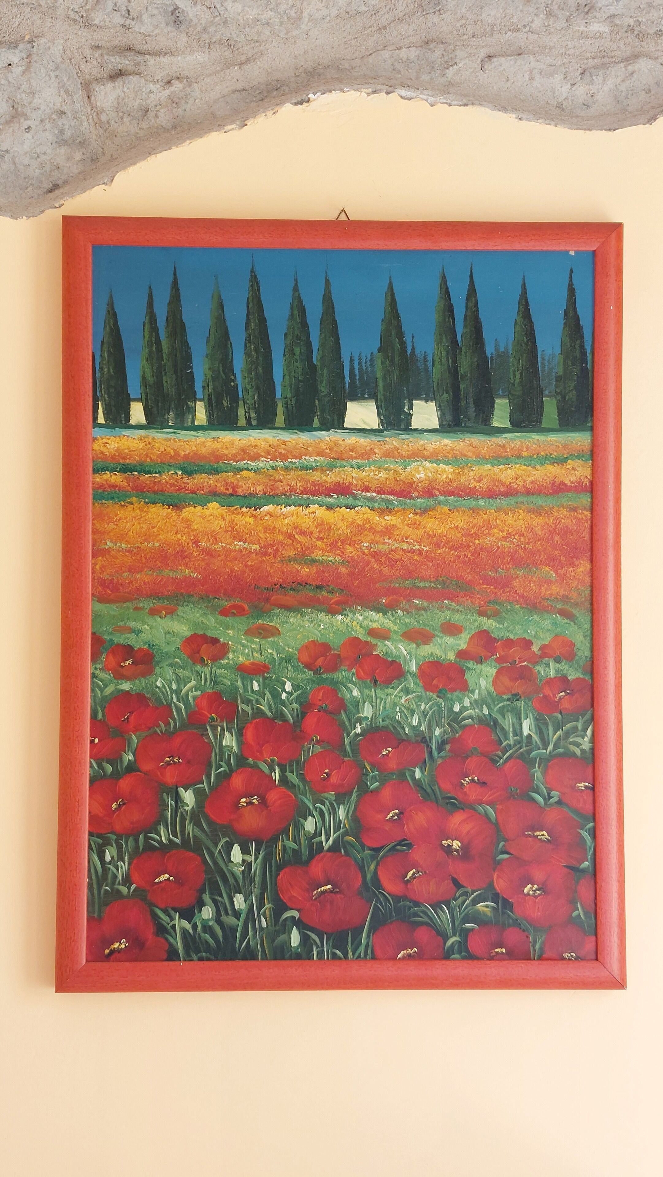Un tableau encadré représentant un champ parsemé de fleurs rouges et bordé de grands arbres.