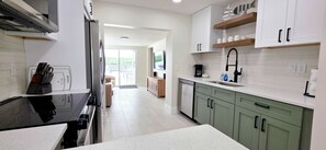 A modern kitchen with a black stove, white cabinets, and a view to the outside. - Private Waterfront House • Private Dock • 2 Min Walk to Beach (Indian Shores)