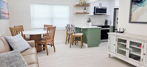 A modern kitchen with white cabinets, a microwave, and a dining area with a table and chairs.