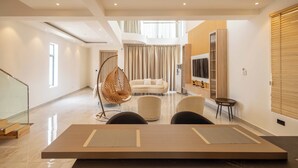 Ein modernes Wohnzimmer mit einer Couch, Sesseln, einem Hängesessel, einem Fernseher und einem Holztisch.