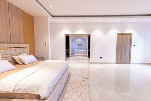 Ein modernes Schlafzimmer mit einem großen Bett, einem Holzkopfteil, einer Marmorwand und einem durchgehenden Türrahmen einsehbarer Badezimmer.