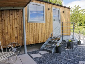 A wooden cabin with a metal staircase leading to a door, a metal bench, and a wheelbarrow. - Little Hut (Grange-over-Sands)
