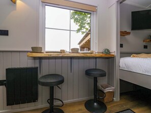 A room with a window, a bed, a TV, and a bar area with stools. - Little Hut (Grange-over-Sands)