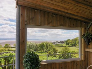 A wooden cabin with a large window offering a view of a lake and greenery. - Little Hut (Grange-over-Sands)