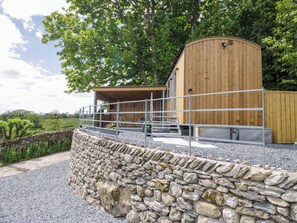 A wooden building with a stone wall in front, a metal fence, and a tree in the background. - Little Hut (Grange-over-Sands)
