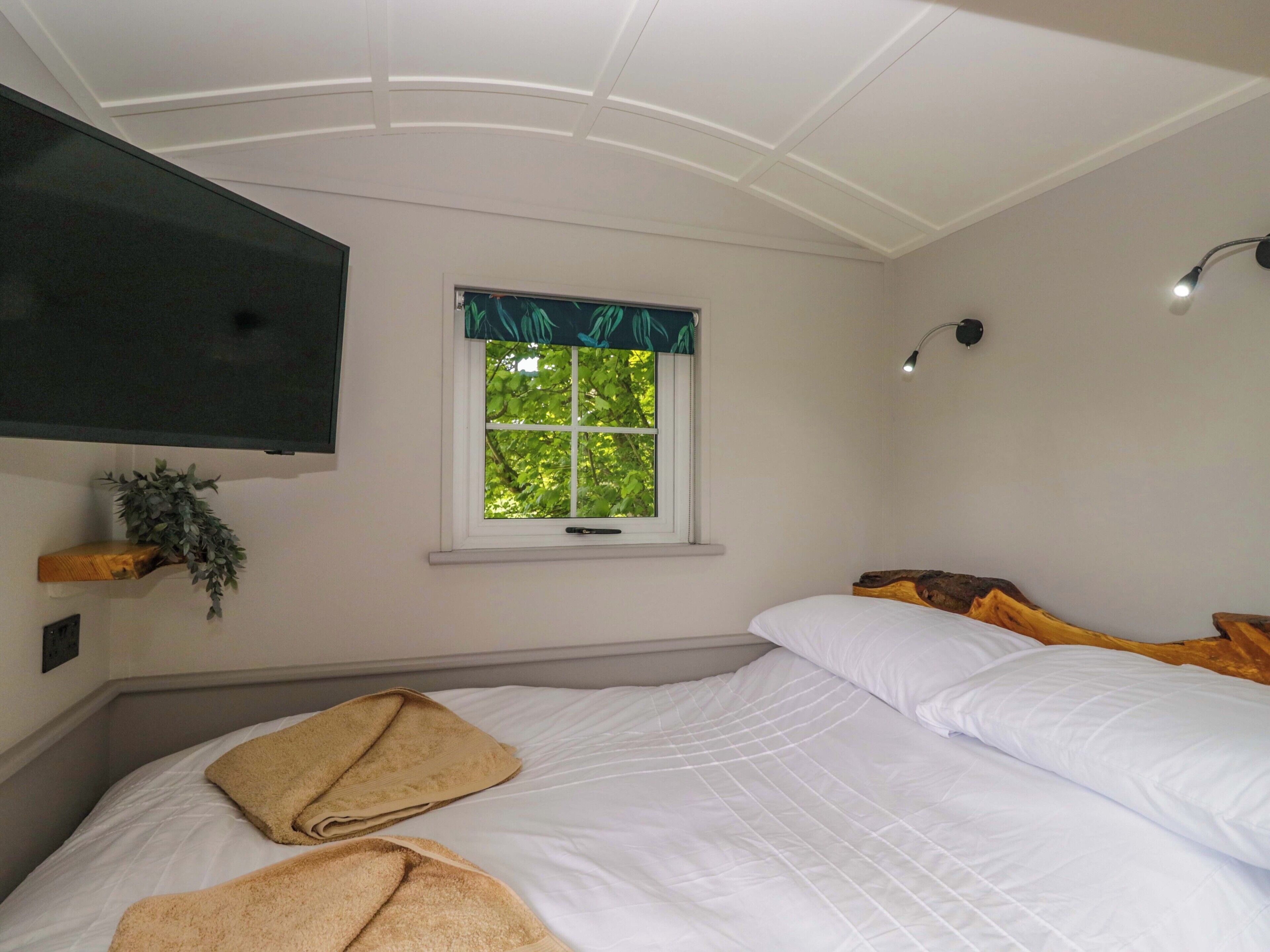 Habitación de hotel con cama, ventana con vistas, televisor montado y lámpara adosada a la pared.