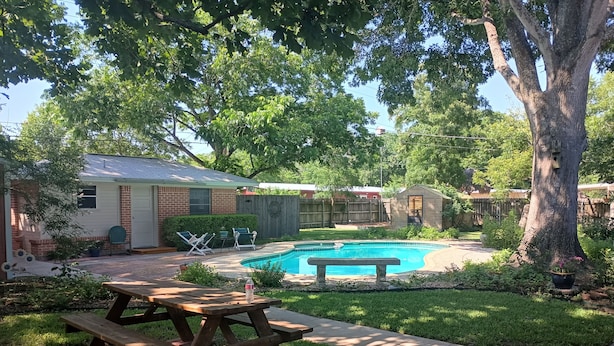 Ein Garten mit Swimmingpool, einem Holzpicknicktisch und einer kleinen Gartenhütte.