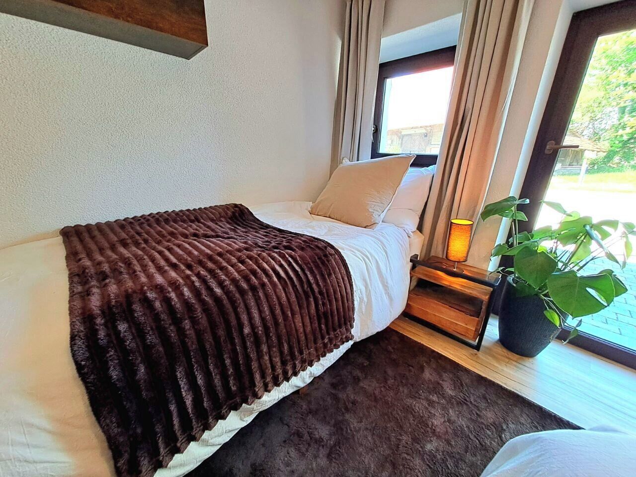 Un letto con una coperta marrone, un comodino con una lampada e una pianta in vaso.